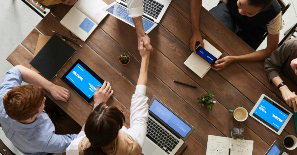 A group of people in a meeting round a table looking at figure on laptops and ipads